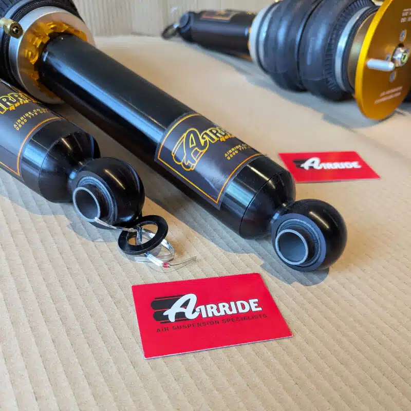 Close up of AirRide Gold Nissan Skyline R33 2WD struts on beige background showing eye connection